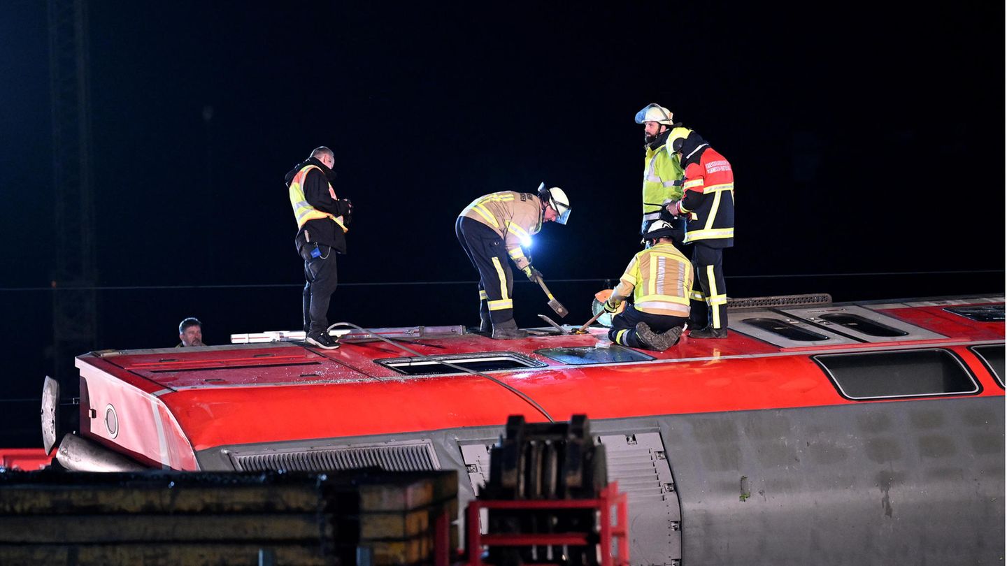 Mehrere Feuerwehrleute stehen mit Vorschlaghammer auf der Seitenwand eines umgekippten Waggons herum
