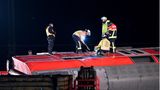 Mehrere Feuerwehrleute stehen mit Vorschlaghammer auf der Seitenwand eines umgekippten Waggons herum