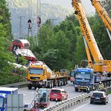 Im Morgenlicht stehen zwei Schwerlastkräne auf einer mehrspurigen Bundesstraße neben dem Gleis mit dem verunglückten Zug