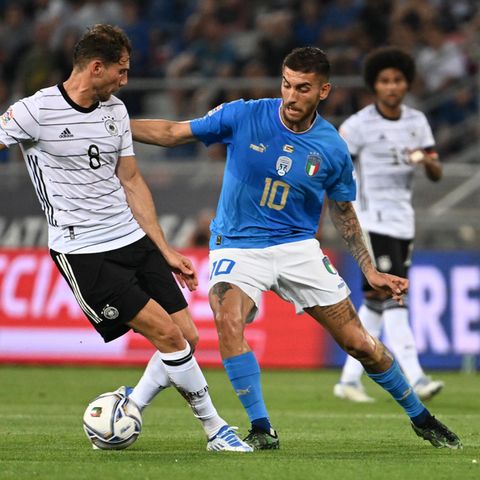 Ein Fußball-Profi in weißem Trikot und schwarzer Hose hat den Ball, ein anderer in blauem Trikot und weißer Hose greift ihn an