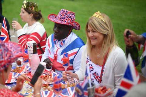 An einer mit Union Jacks geschmückten Tafel sitzen lächelnde Menschen zu einem Picknick zusammen