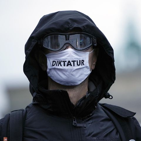 Ein Teilnehmer einer Demonstration trägt eine Mund-Nasen-Bedeckung mit der Aufschrift "Diktatur"