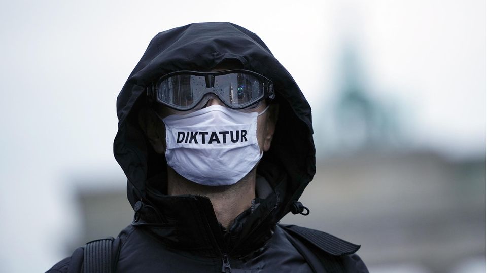 Ein Teilnehmer einer Demonstration trägt eine Mund-Nasen-Bedeckung mit der Aufschrift "Diktatur"