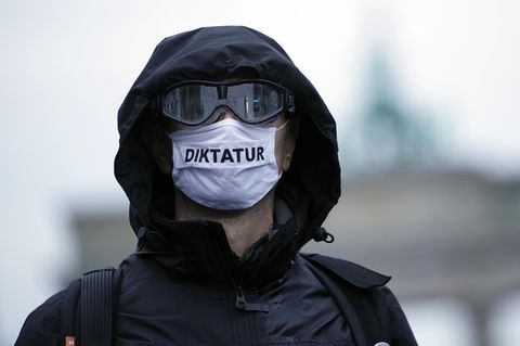 Ein Teilnehmer einer Demonstration trägt eine Mund-Nasen-Bedeckung mit der Aufschrift "Diktatur"
