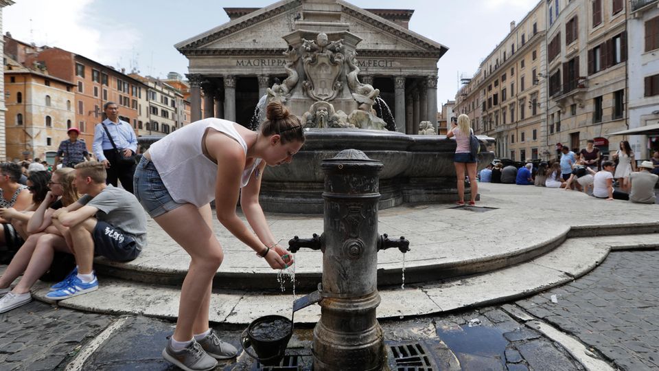 Eine Frau kühlt sich mit dem Wasser aus einem Brunnen ab