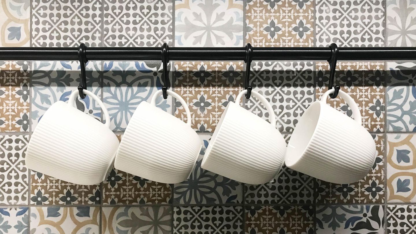 Eine geflieste Wand mit einem Regal, an dem Tassen hängen