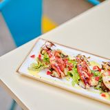 Gefüllte Tintenfischtuben – Kalamária gemistá      Zutaten:  600 g küchenfertige Tintenfischtuben, 2 Zwiebeln, 4 EL Olivenöl, Salz, frisch gemahlener schwarzer Pfeffer, 1 Prise Piment, 50 ml Ouzo, 80 g Basmatireis (oder griechischer Karolina-Reis), 1 EL Pinienkerne, 1 EL Rosinen (nach Belieben), 2 EL gehackte Petersilie, 2 EL gehackter Dill, Saft von 1 Zitrone, 400 g gehackte Tomaten (Dose)  Zum Servieren  Feldsalat      Zubereitung:      Die Tintenfischtuben waschen, trockentupfen und je nach Größe zwei bis drei Tuben in kleine Stücke schneiden. Die Zwiebeln fein hacken.  In einem Topf 2 EL Olivenöl erhitzen, die Zwiebeln hinzugeben und glasig anschwitzen. Die gehackten Tuben unterrühren und mit Salz, Pfeffer und Piment würzen. Alles mit Ouzo ablöschen und anschließend 200 ml Wasser und den Reis unterrühren. Die Mischung unter Rühren köcheln lassen, bis der Reis die Flüssigkeit aufgesaugt hat. Bei Bedarf mehr Wasser hinzugießen.  Sobald der Reis gar ist, den Topf vom Herd nehmen und den Inhalt etwas abkühlen lassen. Pinienkerne, Rosinen, Petersilie und Dill unterrühren.  Den Backofen auf 180 °C Umluft vorheizen. Die Tintenfischtuben mit einer Gabel mehrmals einstechen und mit der Reismischung füllen. Die Öffnung der Tuben mit einem Zahnstocher verschließen. In einem Bräter 2 EL Olivenöl erhitzen und die gefüllten Tintenfischtuben darin kurz rundum anbraten. Mit dem Zitronensaft ab- löschen, gehackte Tomaten hinzugeben und alles im Ofen etwa  30 Minuten backen, bis die Tintenfischtuben weich sind.  In der Zwischenzeit den Feldsalat auf Tellern anrichten. Die Calamari entweder ganz oder in Scheiben geschnitten ohne Zahnstocher auf dem Feldsalatbett anrichten und servieren.