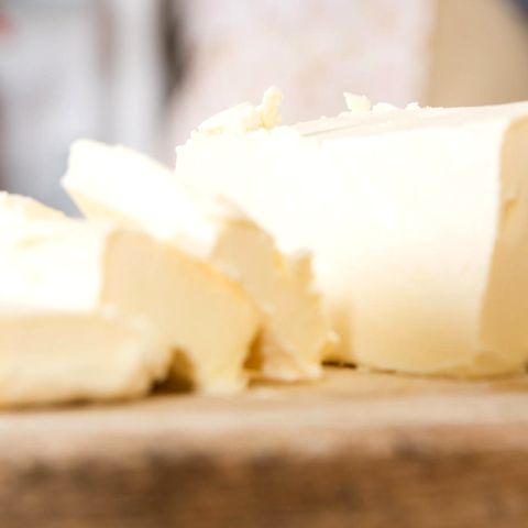 Nahaufnahme von Butterscheiben, im Hintergrund Hausfrau öffnet den Kühlschrank.