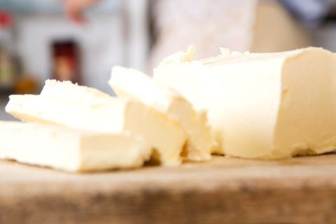 Nahaufnahme von Butterscheiben, im Hintergrund Hausfrau öffnet den Kühlschrank.