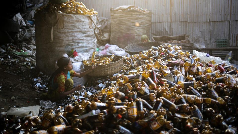 Kinderarbeit: Ein junges Mädchen hockt in Mitte von vielen Plastikflaschen und sortiert sie