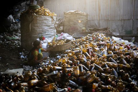 Kinderarbeit: Ein junges Mädchen hockt in Mitte von vielen Plastikflaschen und sortiert sie