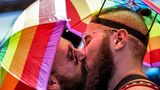 Zwei Männer mit Regenbogen-Schirmhüten küssen sich
