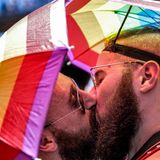 Zwei Männer mit Regenbogen-Schirmhüten küssen sich
