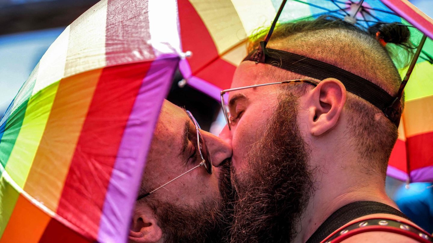 Zwei Männer mit Regenbogen-Schirmhüten küssen sich