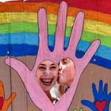 Hinter einem Pappschild gibt eine Frau einer anderen einen Wangenkuss