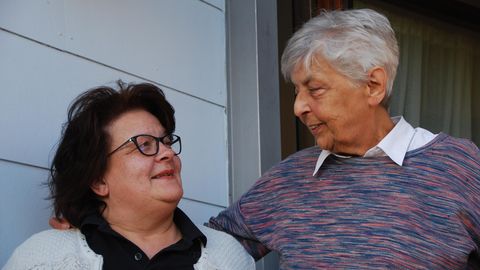 Erwachsenenadoption: Marion Keller und Lotte Coenen stehen nebeneinander vor Coenens Haus und lächeln sich an