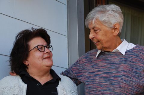 Erwachsenenadoption: Marion Keller und Lotte Coenen stehen nebeneinander vor Coenens Haus und lächeln sich an
