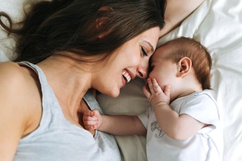 Junge Mutter mit Spaß mit niedlichen Baby-Mädchen auf dem Bett