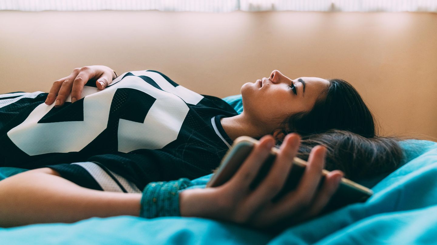 Mädchen liegt mit Handy in Bett