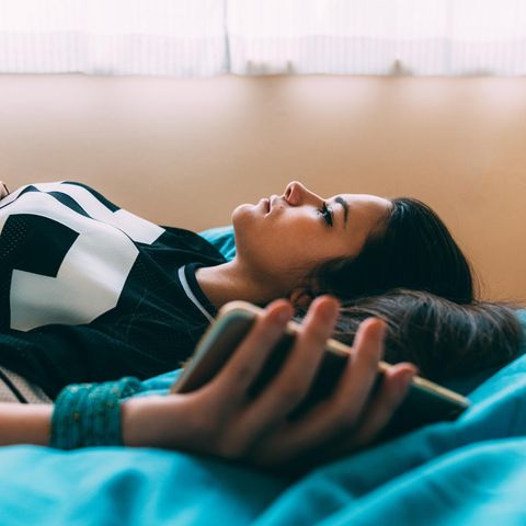 Mädchen liegt mit Handy in Bett