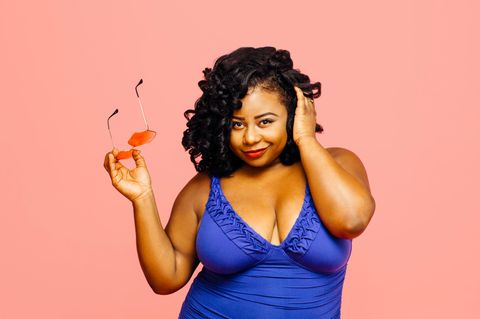 Frau trägt blauen Badeanzug und hält Sonnenbrille in der Hand