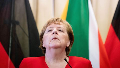 Angela Merkel hebt ernst den Kopf vor Flaggen stehend