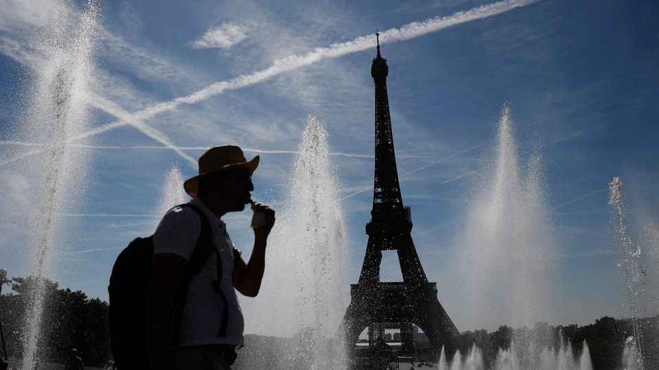 Ein Mann geht an Springbrunnen vor dem Eiffelturm in Paris entlang Ein Mann geht an Springbrunnen vor dem Eiffelturm in Paris entlang