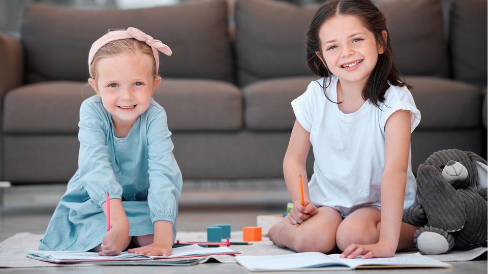 Freundebuch: Zwei Mädchen sitzen lachend mit Stift und Buch auf dem Boden