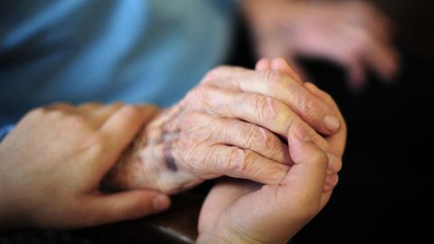 Die Hand einer Pflegefachkraft liegt auf der Hand einer Bewohnerin des Seniorenheims