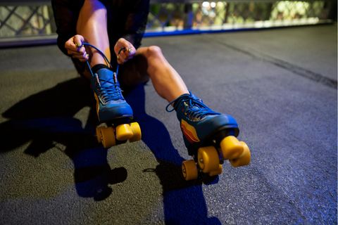 Rollschuhe für Erwachsene: Frau schnürt blau-gelbe Rollschuhe im Sitzen