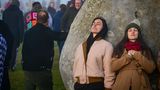 Zwei Frauen lehnen sich an den Heel Stone in Stonehenge