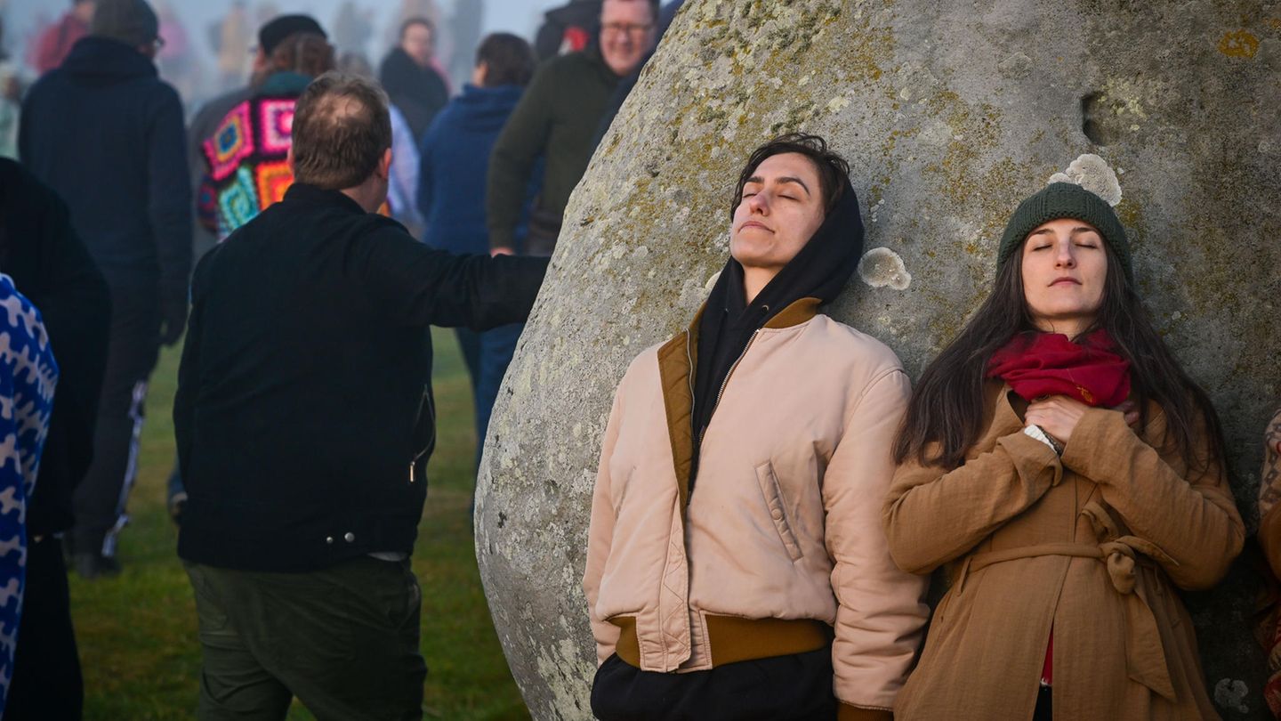 Zwei Frauen lehnen sich an den Heel Stone in Stonehenge