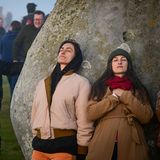 Zwei Frauen lehnen sich an den Heel Stone in Stonehenge