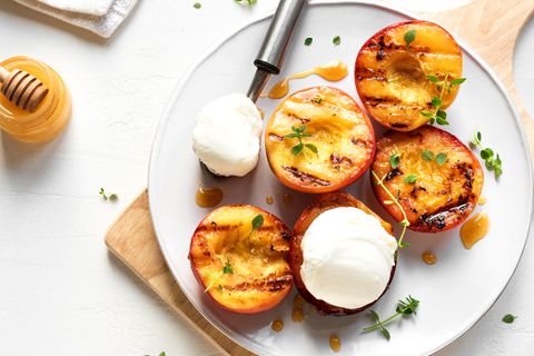 Gegrillte Pfirsiche mit Thymian, Honig und einer Kugel Vanilleeis auf weißer Platte