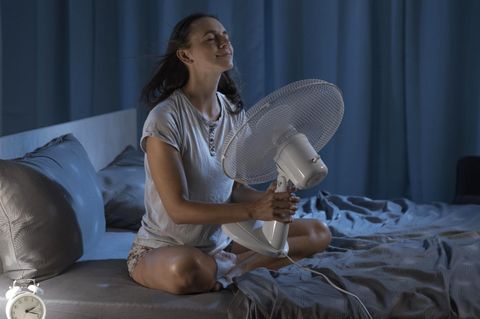Frau in ihrem Schlafzimmer in einer heißen Sommernacht, sie genießt frische Luft vor einem Ventilator