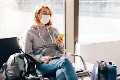 Eine Frau sitzt wartend am Flughafen und schaut auf ihr Telefon