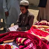 Ein Junge liest aus einem religiösen Buch neben der in eine Decke gewickelten Leiche eines Erdbebenopfers