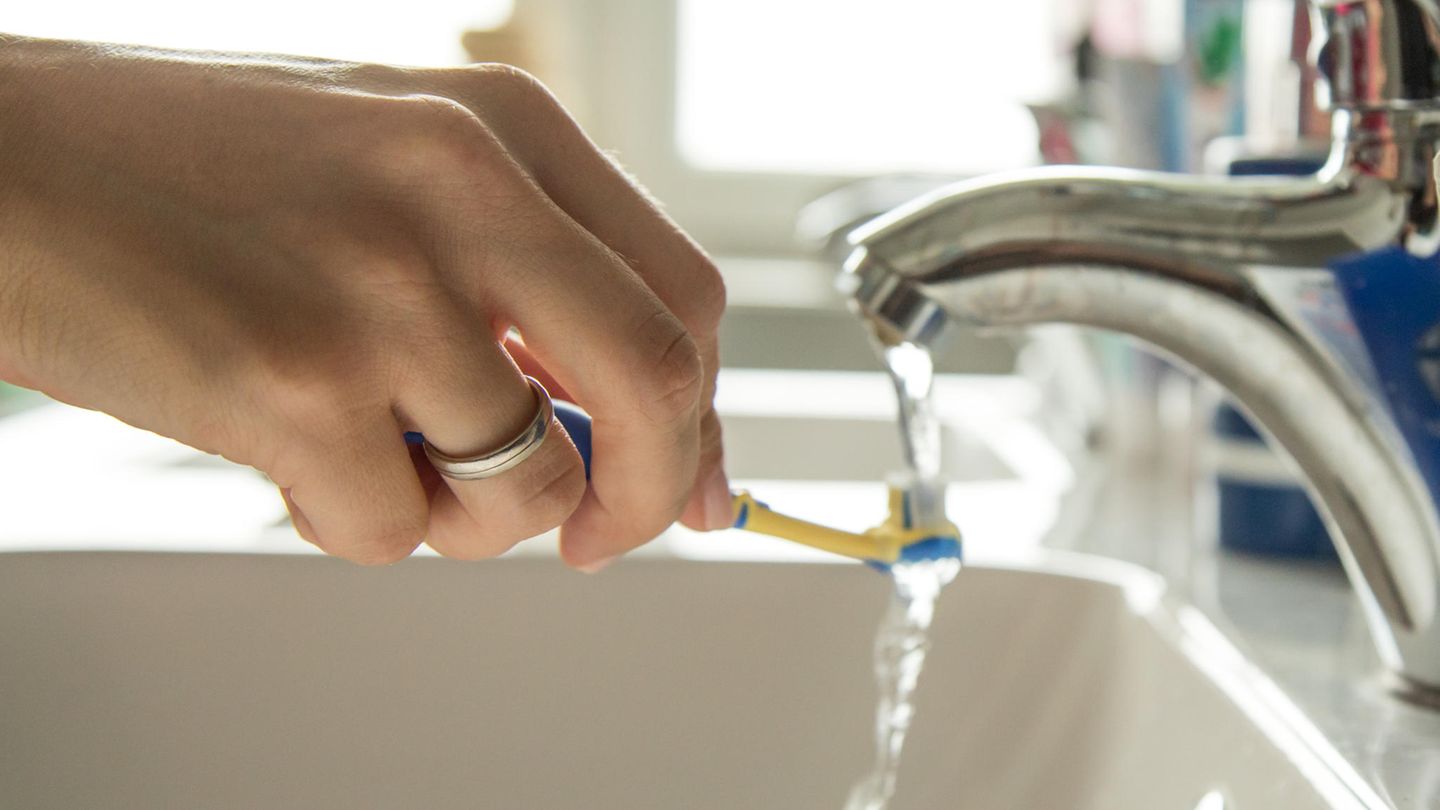 Frau hält eine Zahnbürste unter einen laufenden Wasserhahn