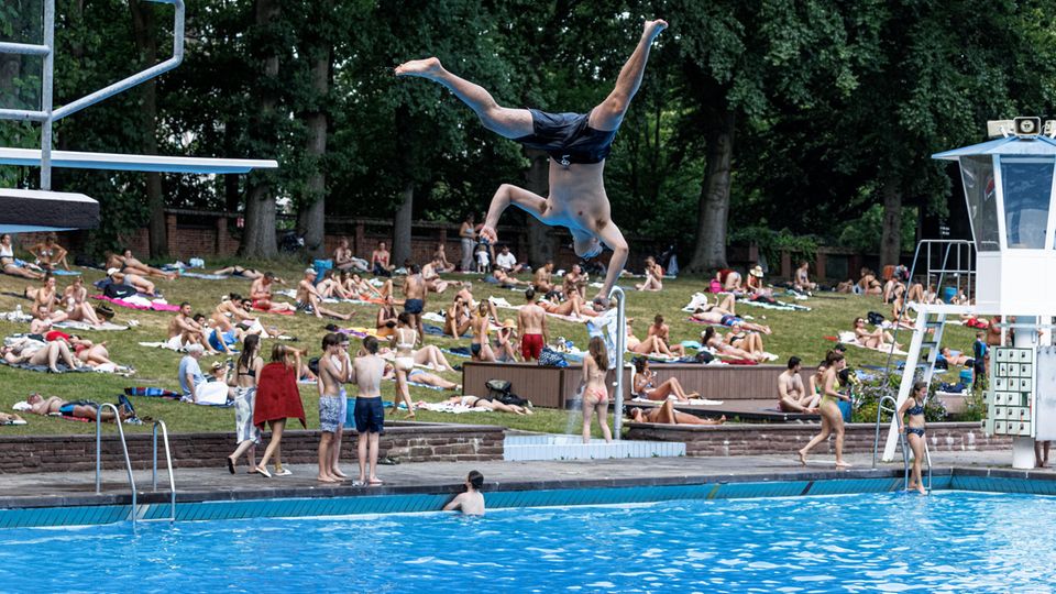 Ein junger Mann springt im Freibad von einem Sprungbrett ins Wasser