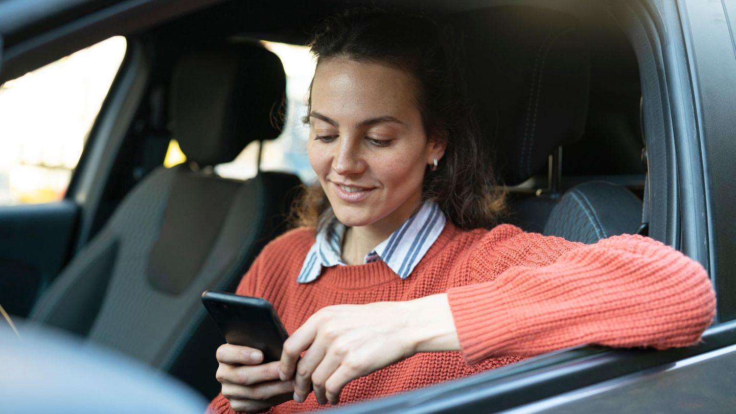 Eine junge Frau sitzt am Steuer und sucht auf ihrem Smartphone nach Tankstellen