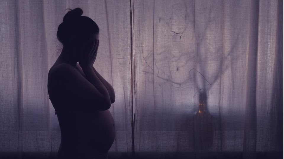 Eine traurige Schwangere steht am Fenster