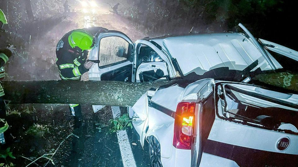 Österreich Unwetter Ein Feuerwehrmann leuchtet mit Taschenlampe in ein Auto, auf das ein Baum gestürzt ist