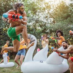 Wasserpistole für Erwachsene: Junge Menschen beschießen sich in einem Park mit Wasserpistolen