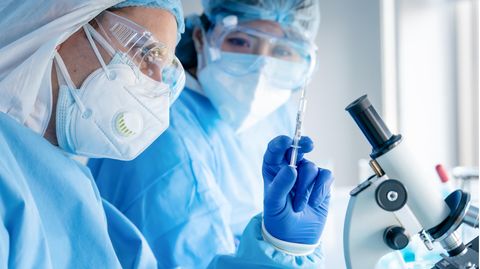 Zwei Labormitarbeiter betrachten eine Spritze für die Impfstoffentwicklung