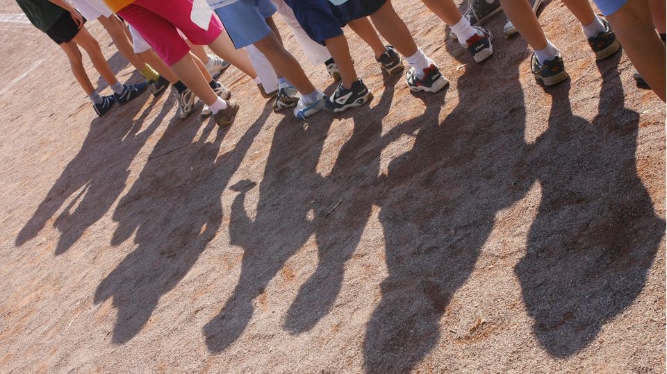 Fulda: Mehrere Kinder stehen aufgereiht auf einem Sportplatz hintereinander, nur ihre Beine und ihre Schatten sind zu sehen