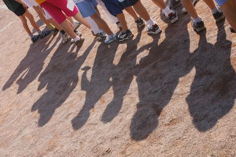 Fulda: Mehrere Kinder stehen aufgereiht auf einem Sportplatz hintereinander, nur ihre Beine und ihre Schatten sind zu sehen