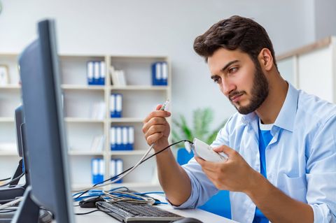 Ein junger Mann hält einen Router und ein Kabel in der Hand