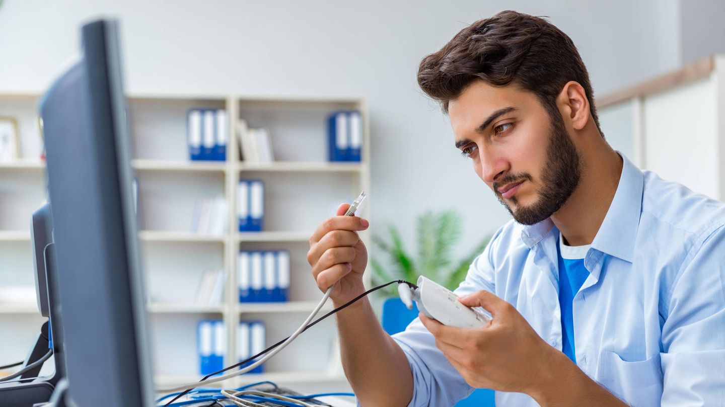 Ein junger Mann hält einen Router und ein Kabel in der Hand