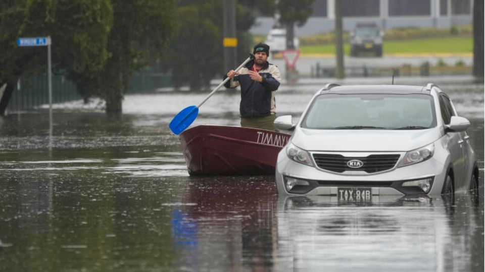 Ein Mann paddelt mit seinem Boot auf einer überfluteten Straße am Stadtrand von Sydney