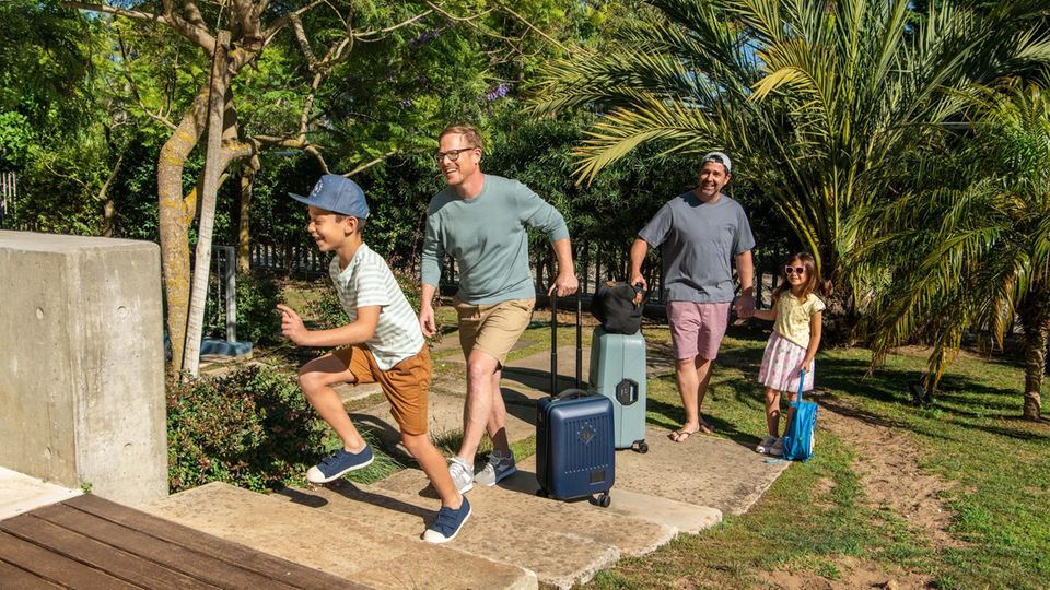 Schwules Paar mit Kindern kommt mit Koffern in einem Hotel an